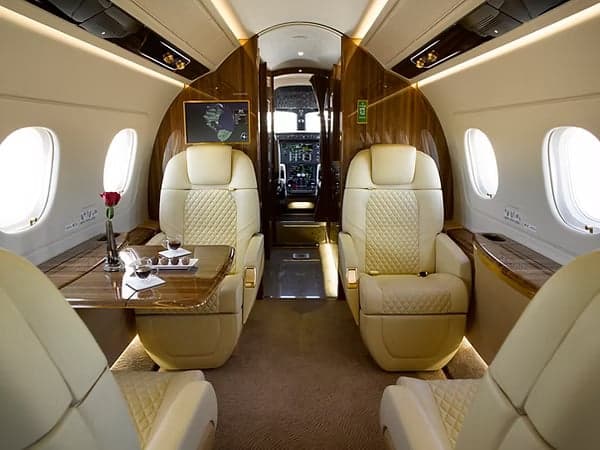 A view of the interior of the aircraft with cream-colored leather seats and a wooden table.