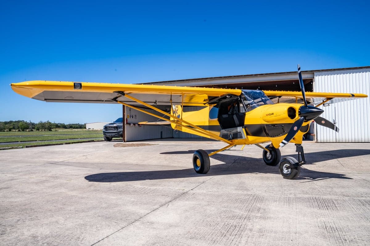Yellow and black NX Cub aircraft parked outside a hangar.