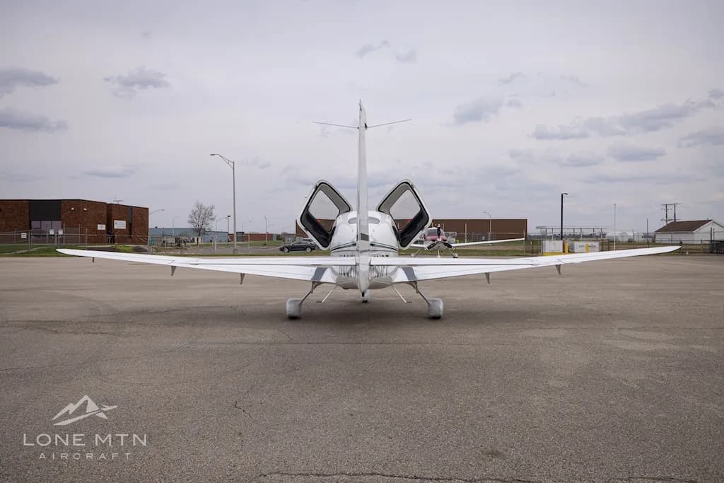 A rear view of a white Cirrus SR22 aircraft with its doors open, parked on an asphalt ramp.