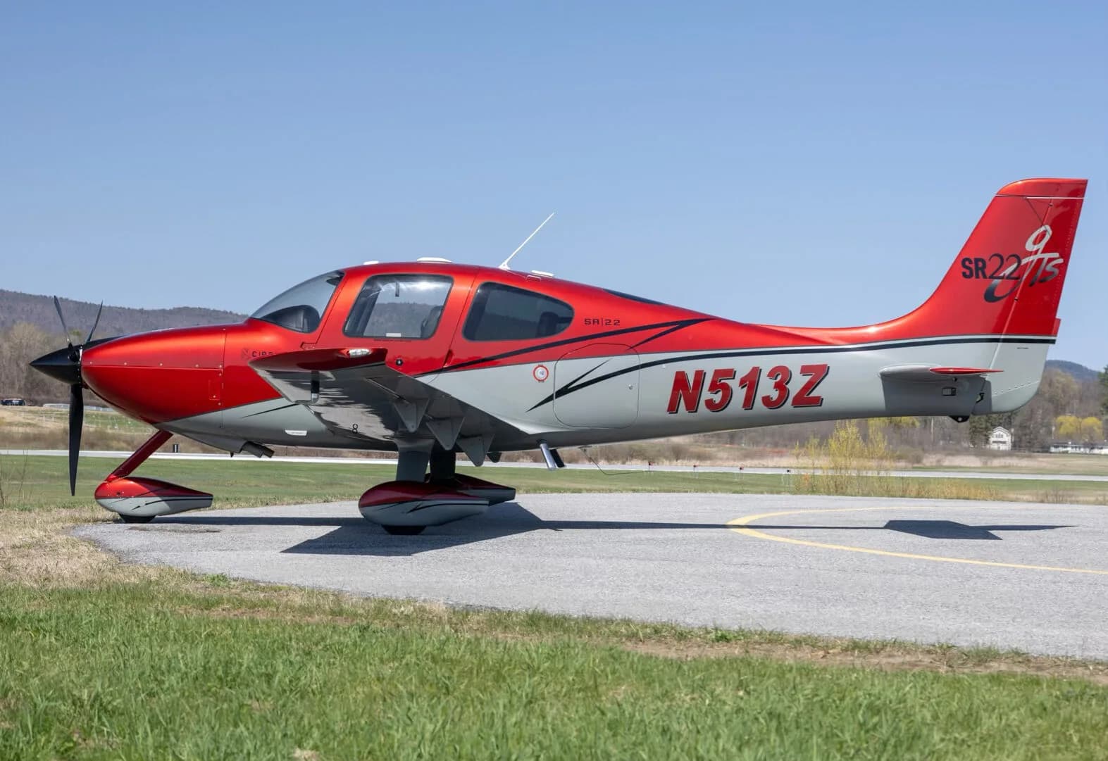 A red and grey Cirrus SR22T aircraft (N513Z) parked on an asphalt runway, side view.