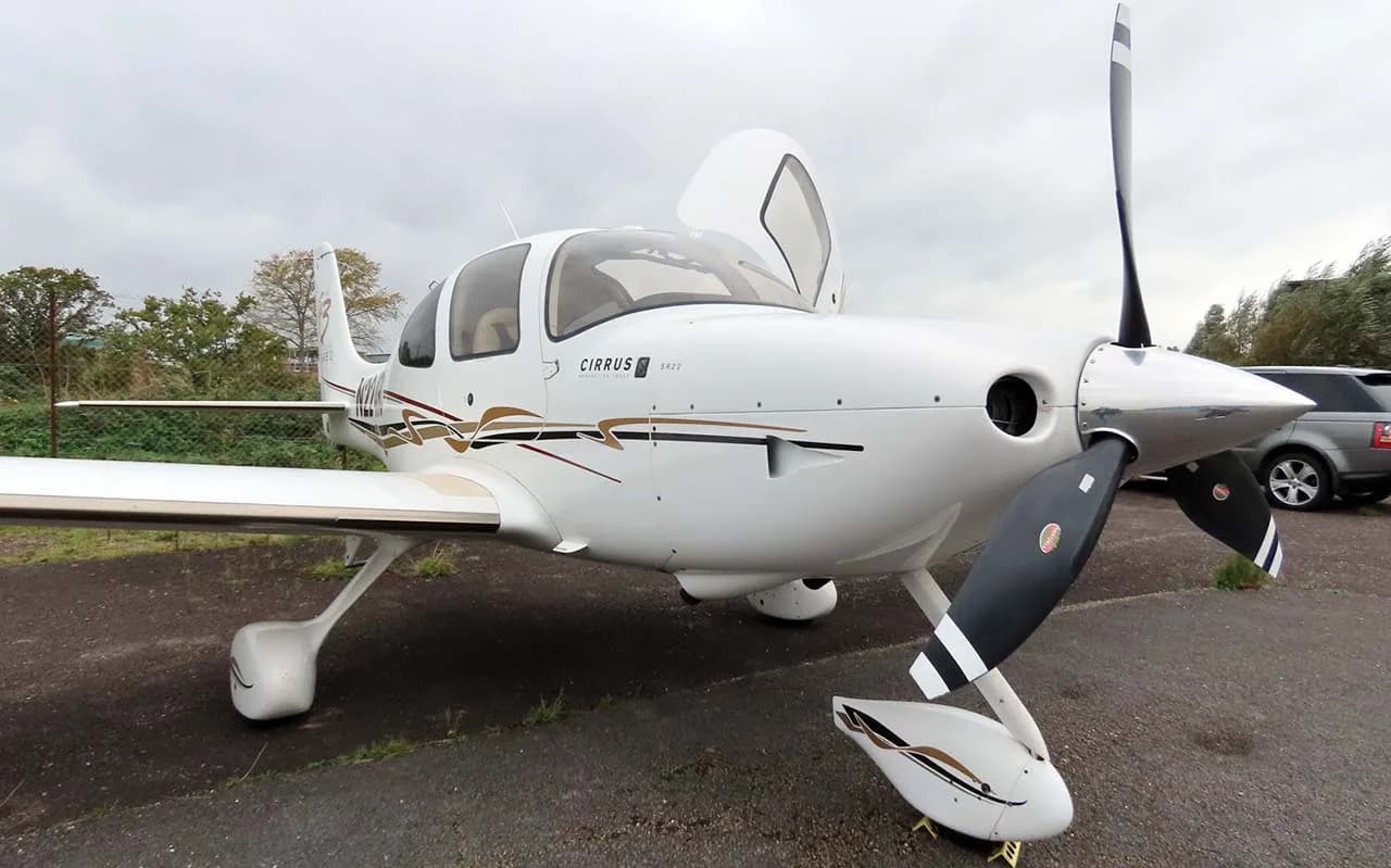 A front-quarter view of a white Cirrus SR22T (N224RC) with its doors open, parked on an asphalt surface.