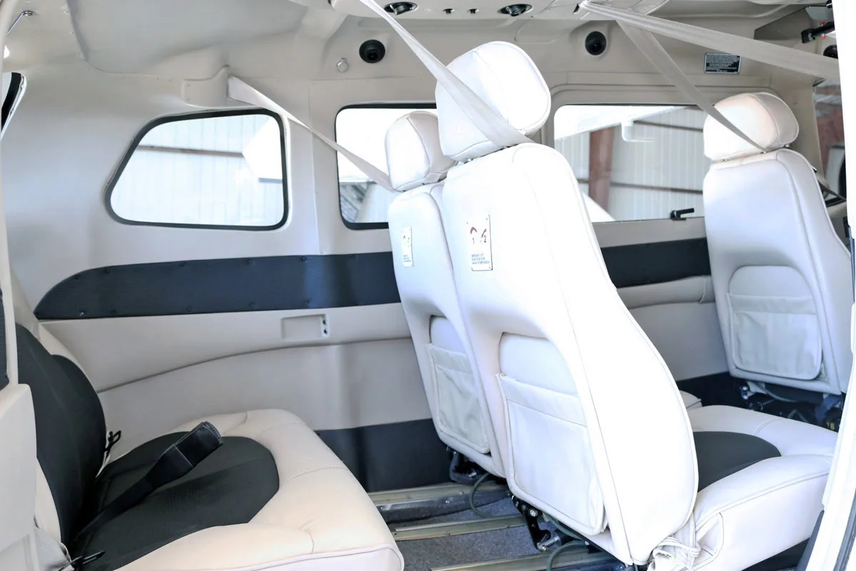The interior cabin of a Cessna Stationair TC aircraft, showing white and black leather seats with seatbelts.