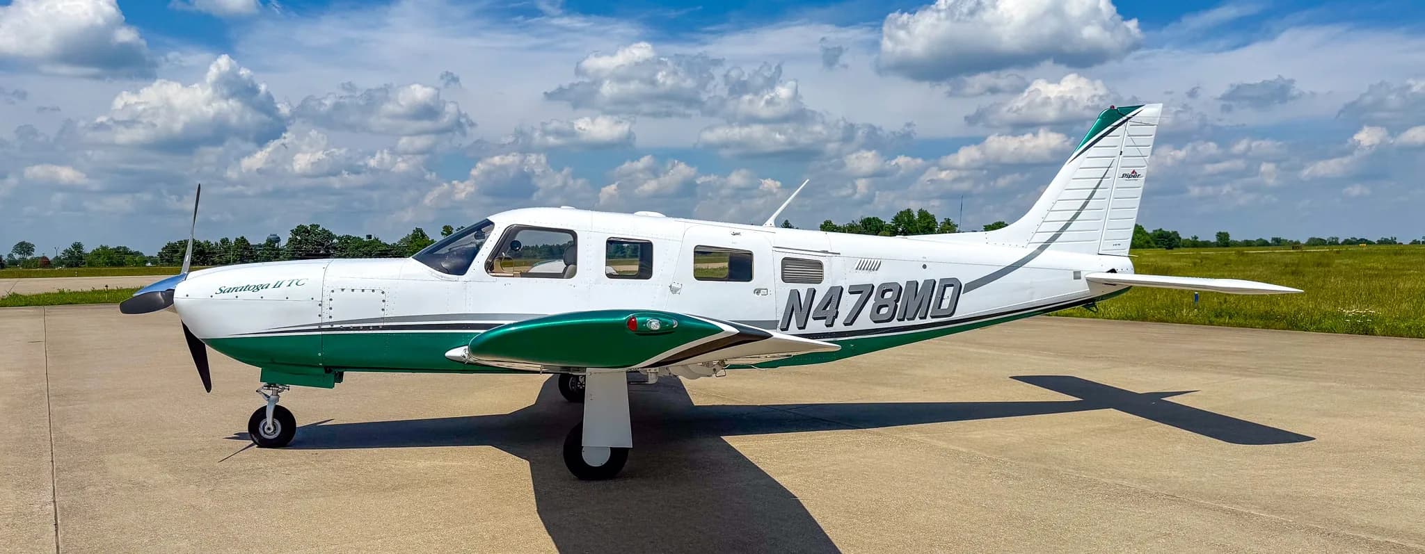 A side view of the white and green Piper Saratoga II TC aircraft (N478MD) parked on an airfield.