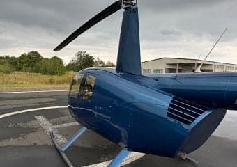 A blue Robinson R44 helicopter on a helipad, viewed from the rear.