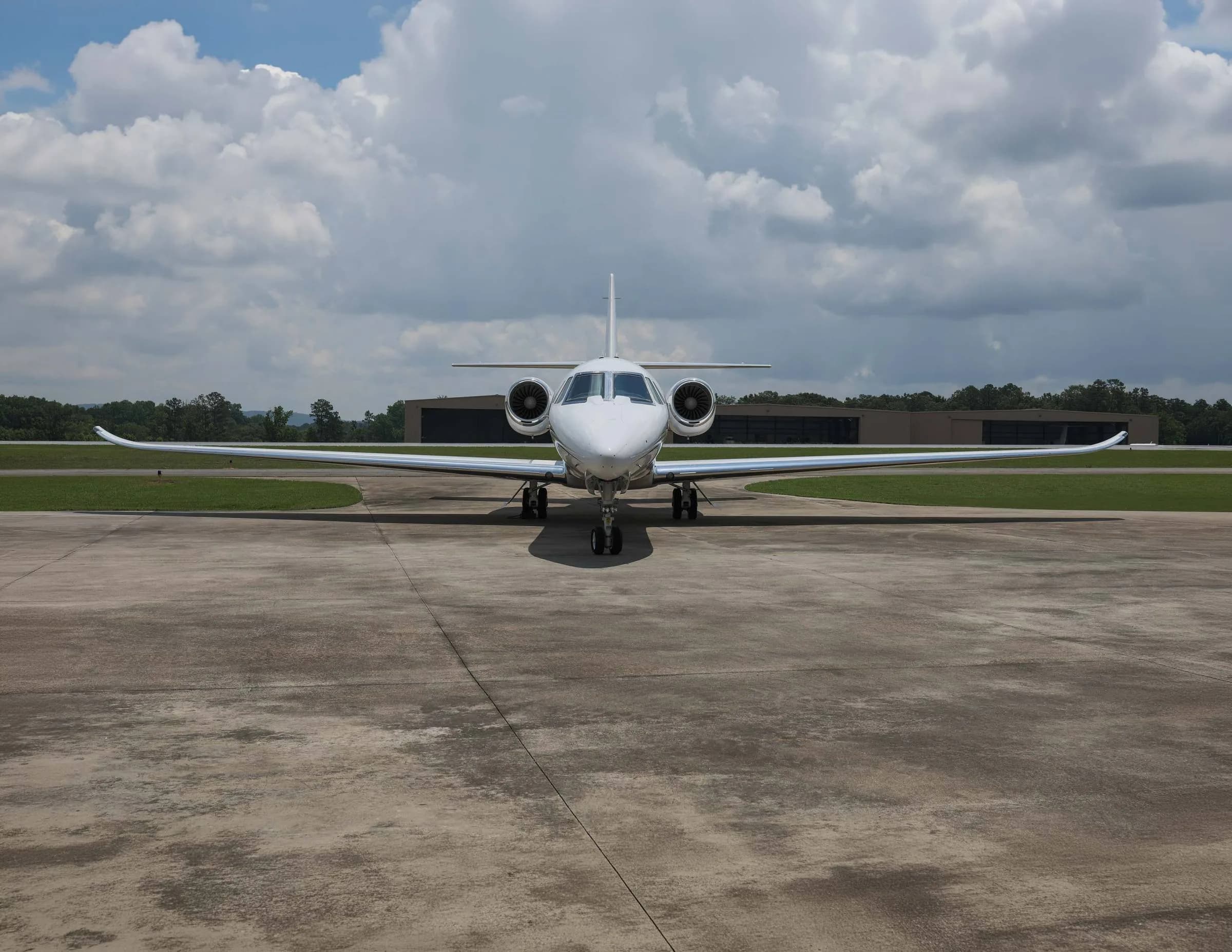 A head-on view of a white business jet with black stripes parked on an airfield.