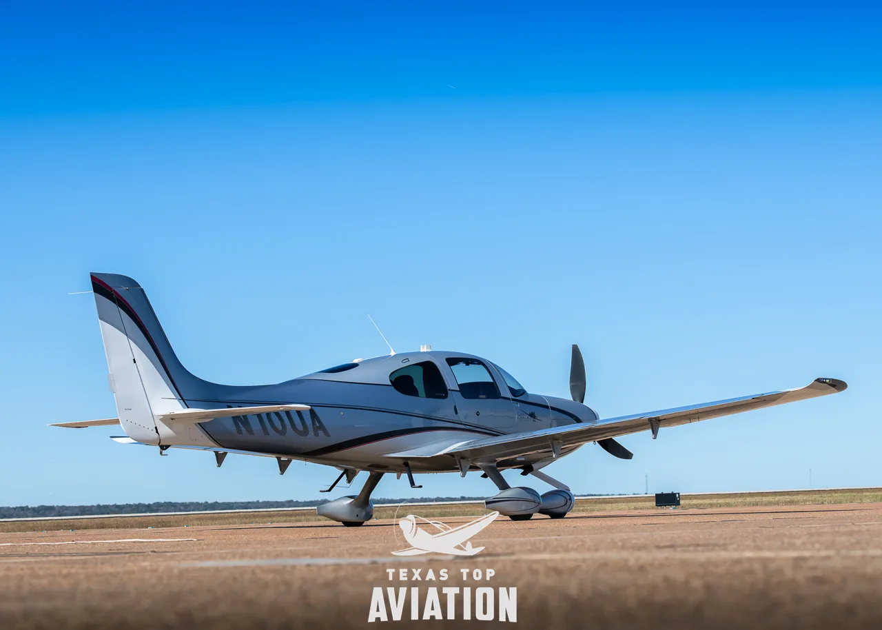 Side-rear view of a silver and white Cirrus SR22 aircraft (N10UA) on an airfield.