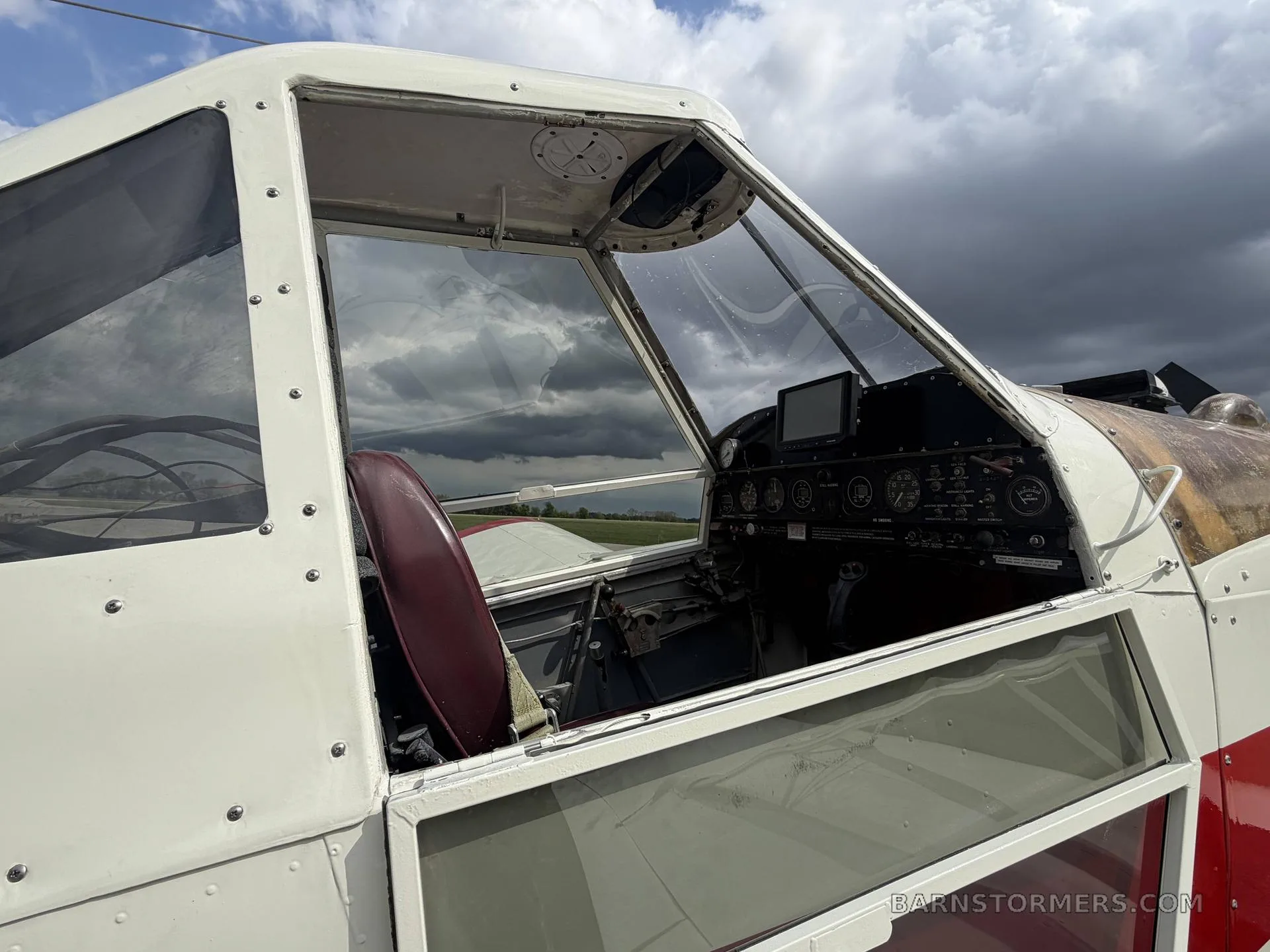 The cockpit interior of a white and red agricultural aircraft, showing the instrument panel and seat.