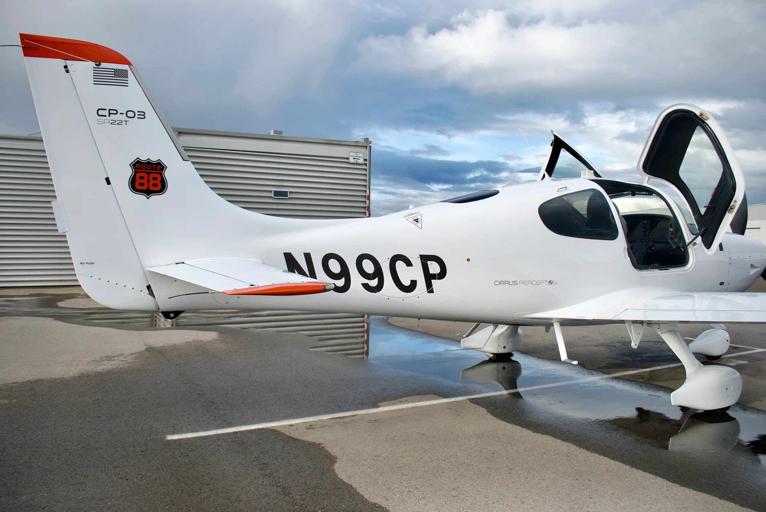 The rear-left side of a white Cirrus SR22T aircraft with registration N99CP, showing the tail with a "ROUTE 88" logo and an open door.