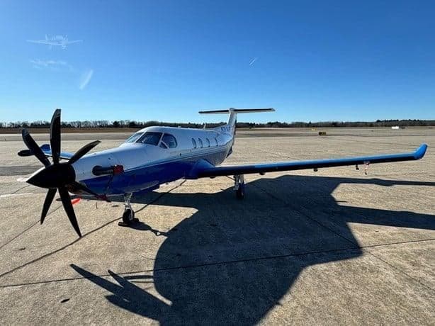 A Pilatus PC-12 aircraft with a blue and white paint scheme is parked on the tarmac.