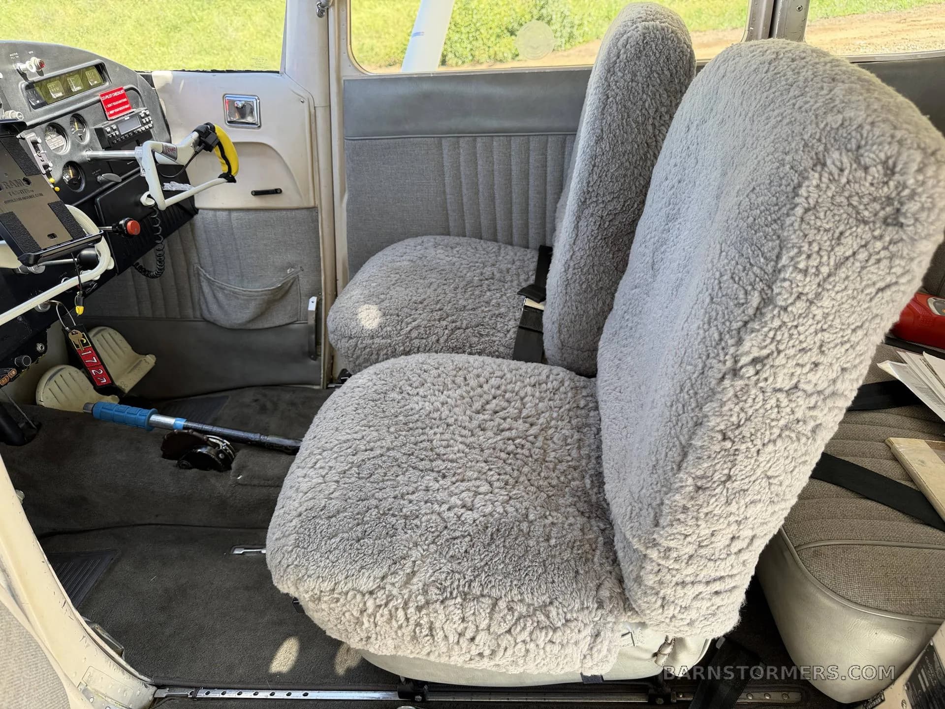 The interior of an aircraft cabin, showing two front seats covered in grey sheepskin-like material.