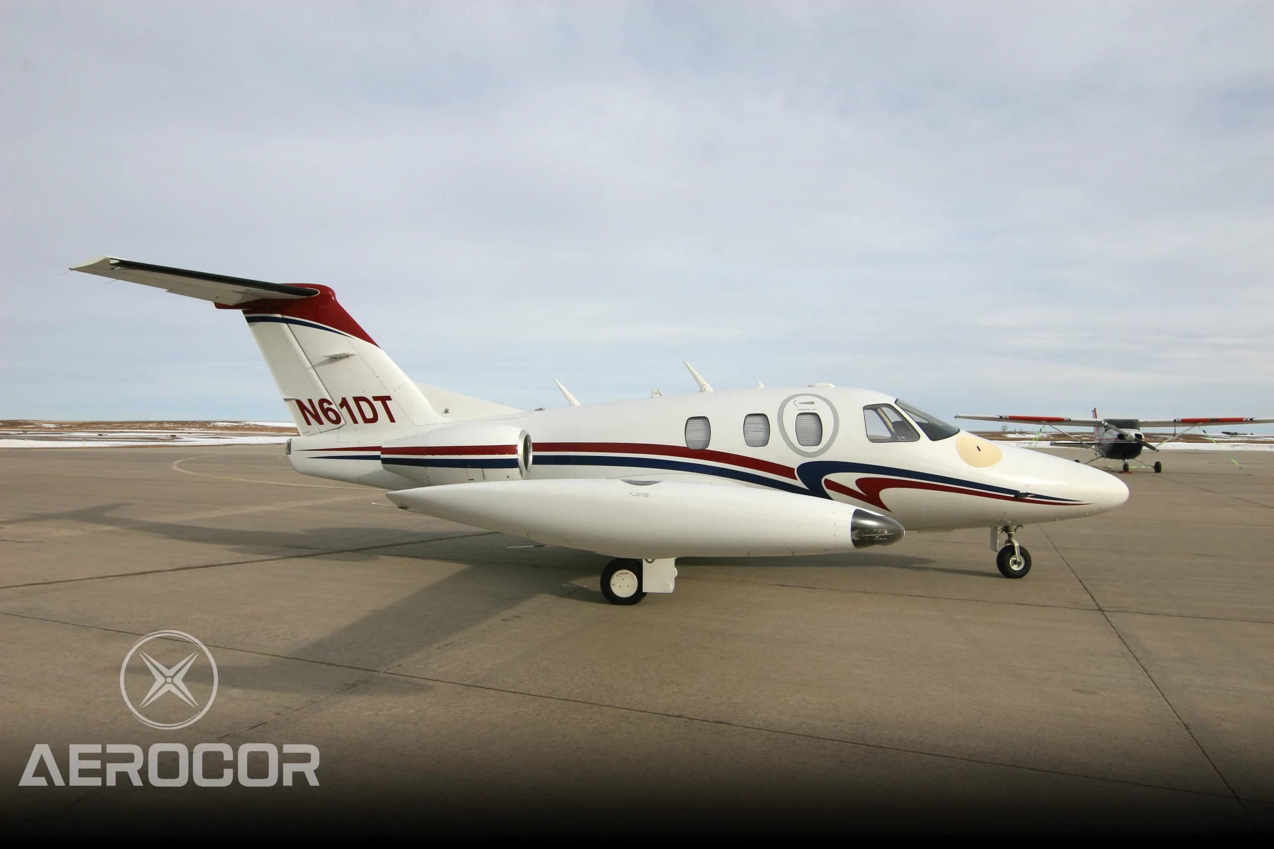 A white Eclipse 500 jet with red and blue stripes parked on an airport tarmac, viewed from the right side.