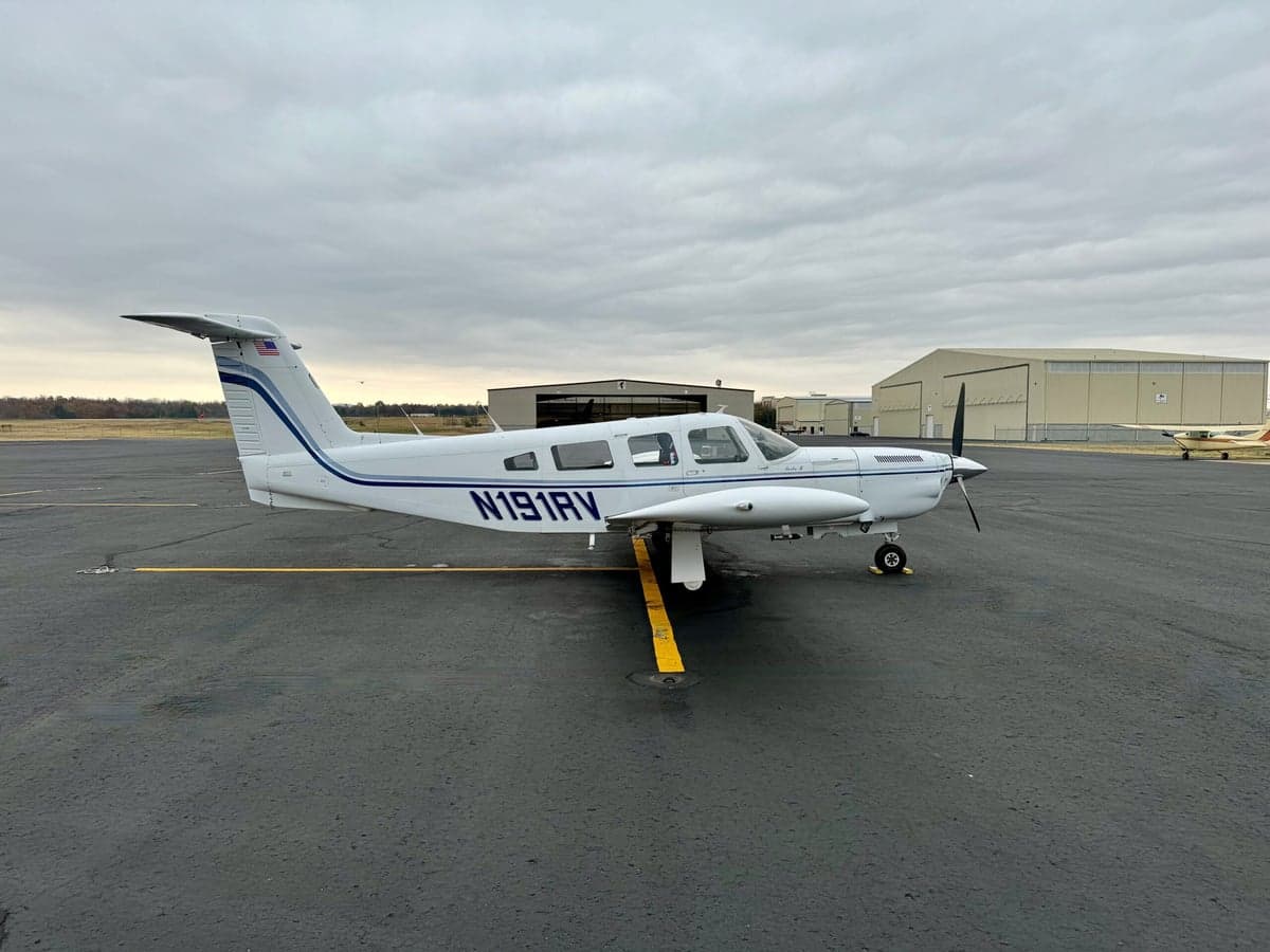 Three-quarter rear view of a white single-engine propeller aircraft with blue stripes and registration N191RV on an airfield.
