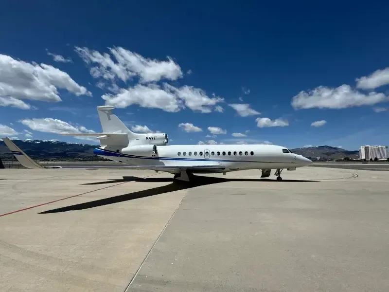 Side view of a Falcon aircraft with a white and blue paint scheme on the tarmac.