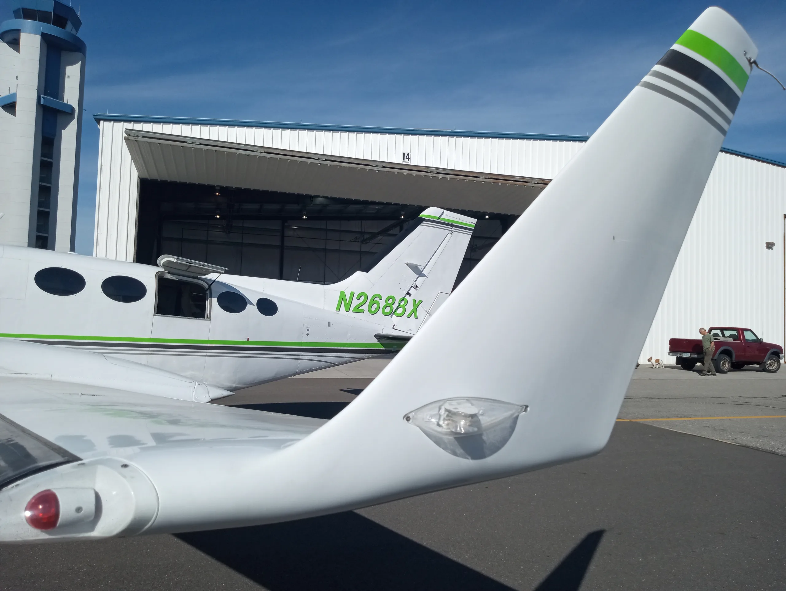 A view of the white tail and wingtip of the N2688X aircraft, with a control tower and hangar in the background.