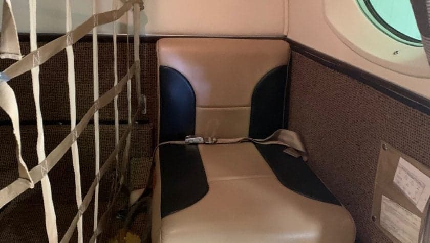 Close-up of a passenger seat in the aircraft's interior, showing the seatbelt and side panel.