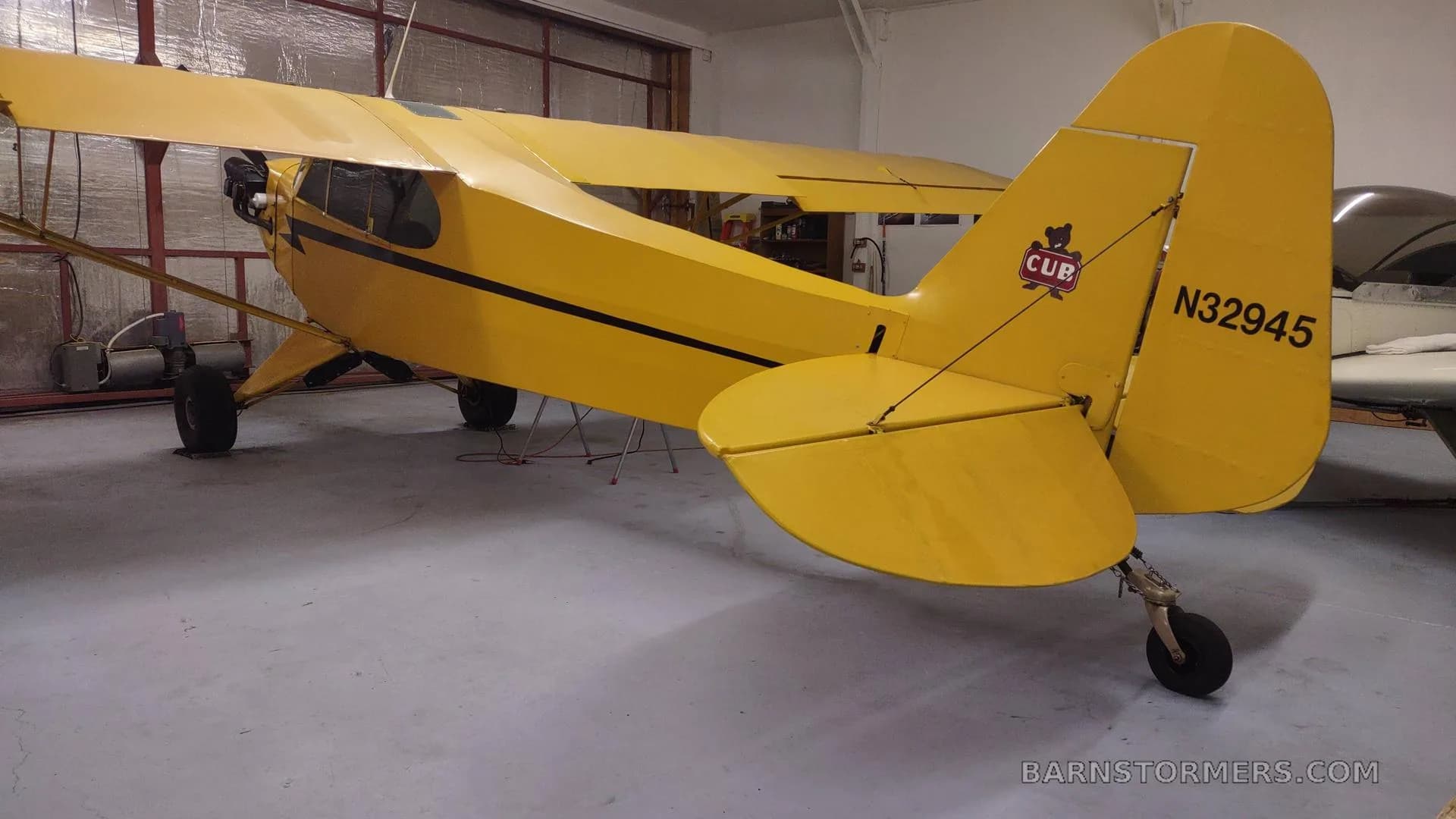 A yellow Piper Cub aircraft with registration N32945 is parked in a hangar, viewed from the rear right.