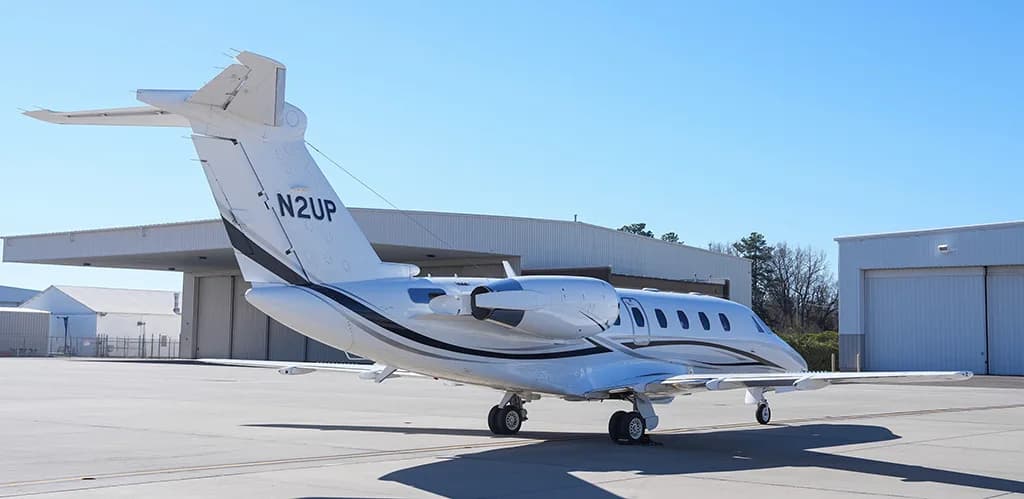 A white Cessna Citation business jet with black and grey stripes, registration N2UP, parked on an airfield from a rear-quarter view.