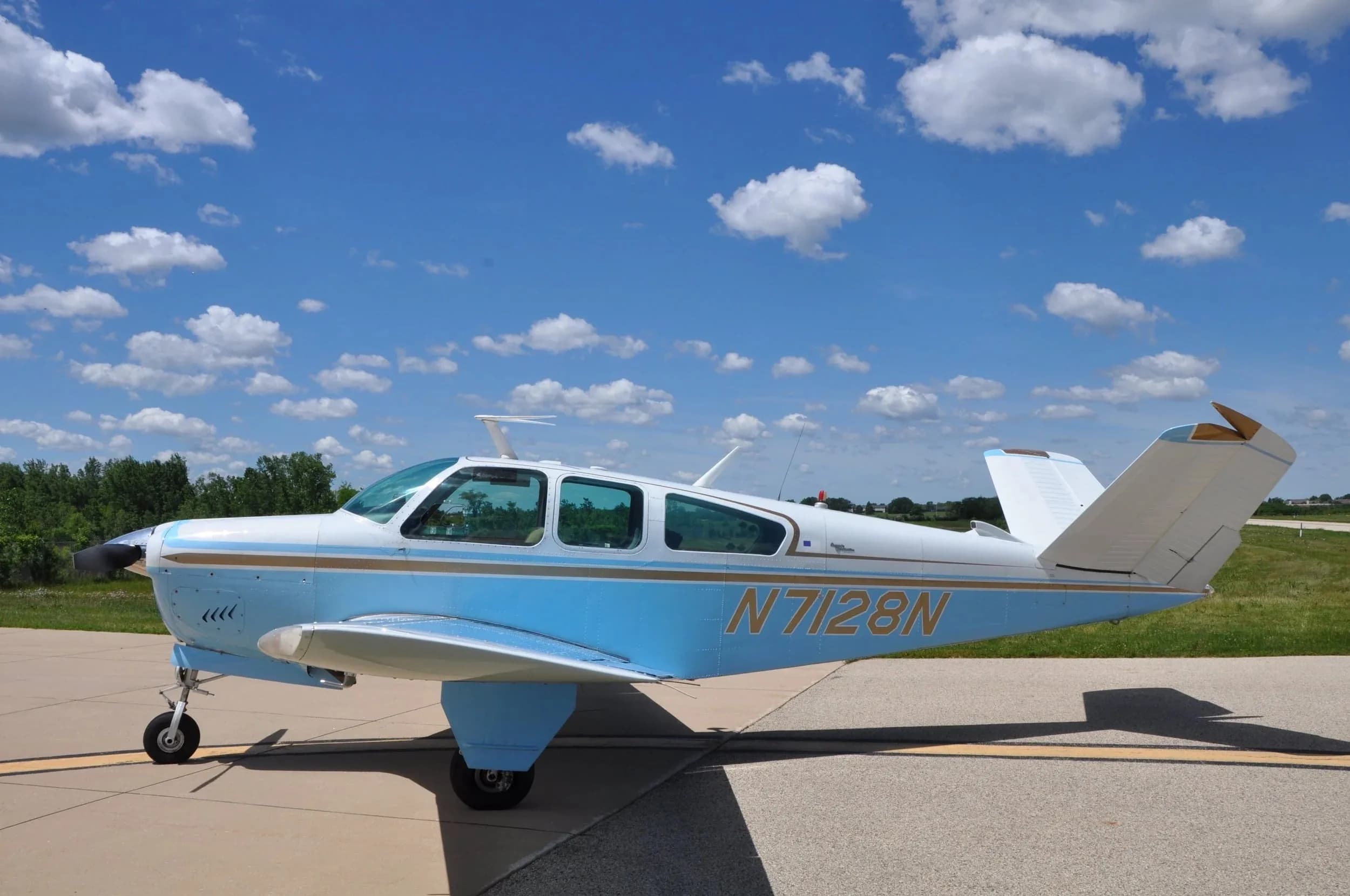 A side view of the light blue and white Beechcraft Bonanza N7128N parked on an airfield.