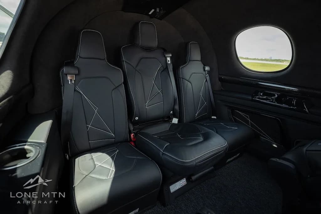 The black leather interior of a Cirrus Vision Jet cabin with three passenger seats and a window view of the tarmac.