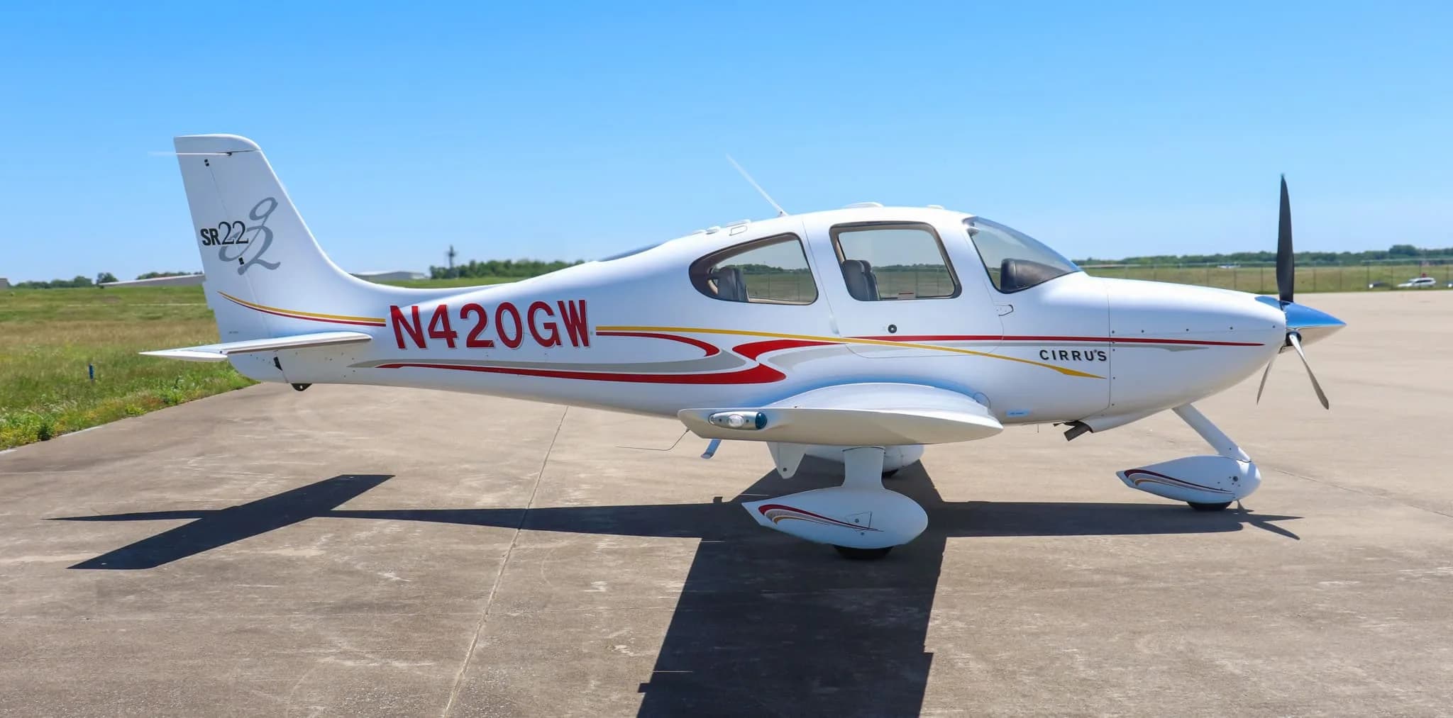 Front-right view of a white Cirrus SR22 aircraft with red and gold stripes on a tarmac.