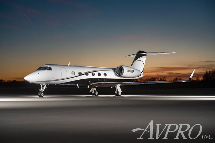A white and black Gulfstream G550 (N986SP) parked on a tarmac at sunset with runway lights illuminating the ground.