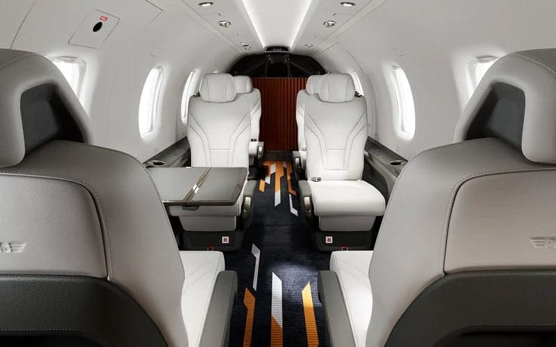 View of the Pilatus PC-12 cabin with white leather seats and a table.