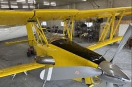 A yellow biplane crop duster is parked inside a hangar.