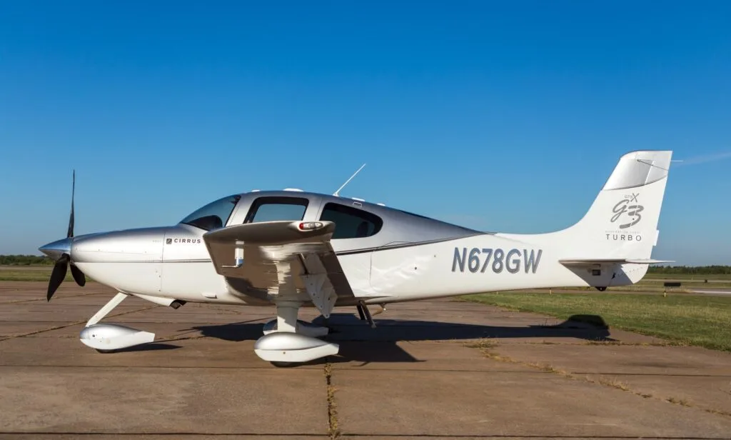 A side view of a silver and white Cirrus SR22 G3 Turbo aircraft (N678GW) parked on an airfield.