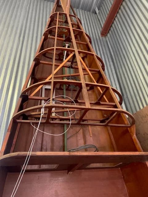 An upward view of the intricate wooden skeletal frame of an aircraft fuselage.