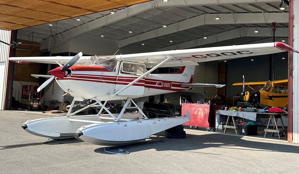 A Cessna floatplane with red and white paint scheme is parked in a hangar.