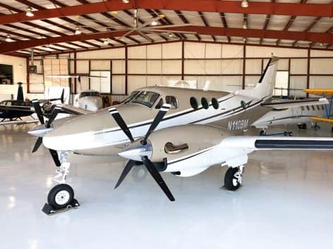 A tan and white twin-engine turboprop aircraft, N110BM, parked inside a hangar.