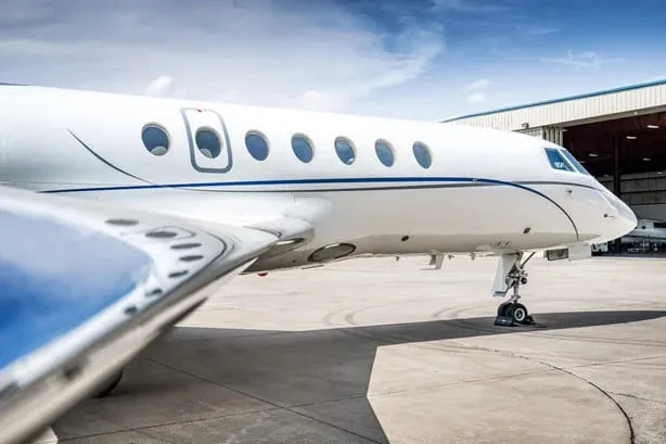 A close-up side view of the fuselage and wing of a white business jet with blue stripes, parked on an apron.