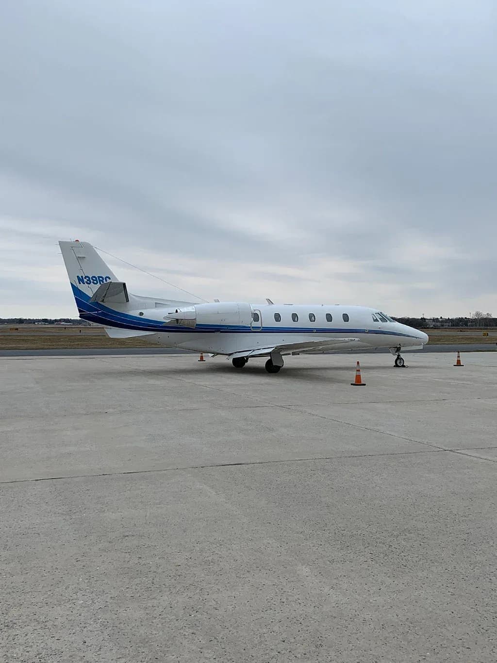 Side profile of a white business jet with blue stripes and registration N39RC parked on an airfield.
