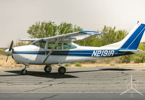 A white Cessna 182 with blue stripes and tail number N2191R is parked on an airfield.