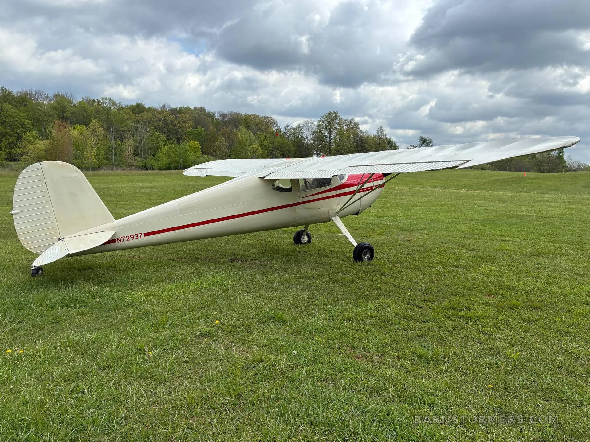 A rear-side view of the white and red single-engine aircraft with taildragger landing gear on a grassy field.