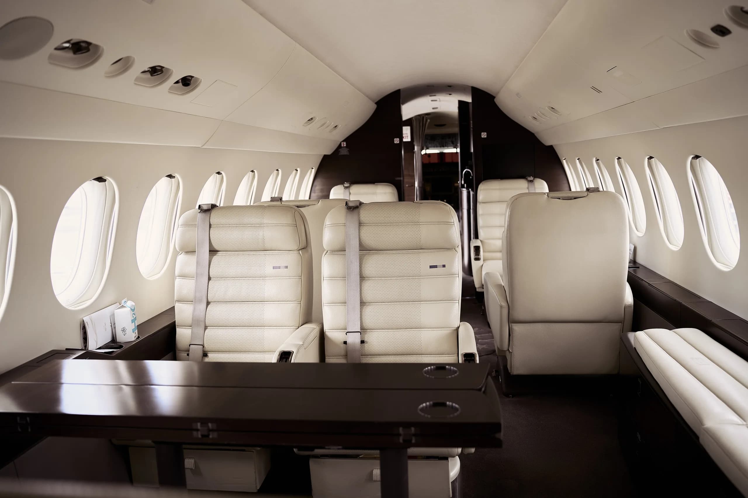 View of a luxurious aircraft cabin with light cream leather seats and a dark wooden table.