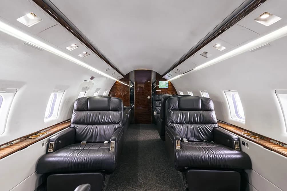 The luxurious interior cabin of a private jet, featuring black leather seats and wood paneling.