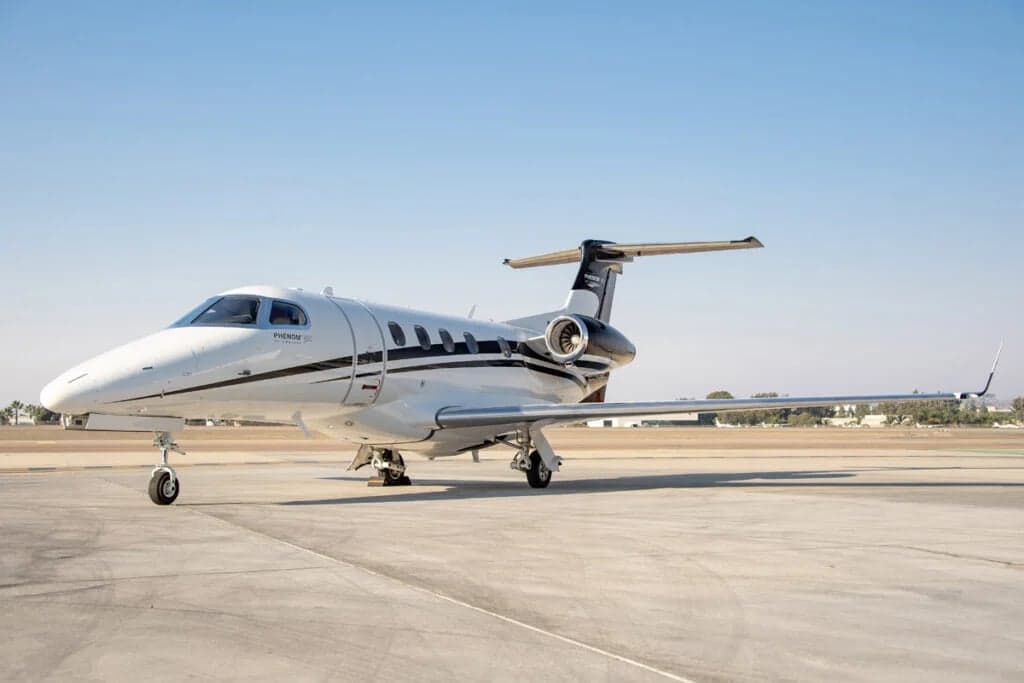 A Phenom 300 aircraft with a white and black paint scheme is parked on the tarmac.
