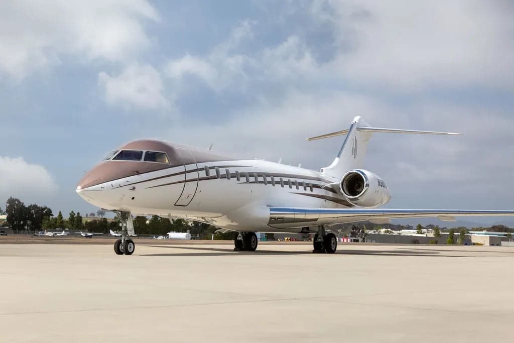 A Bombardier Global Express aircraft with a brown and white paint scheme parked on the tarmac.