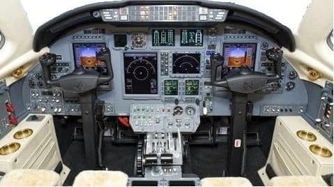 The cockpit of a business jet features a modern glass panel with multiple displays and two control yokes.