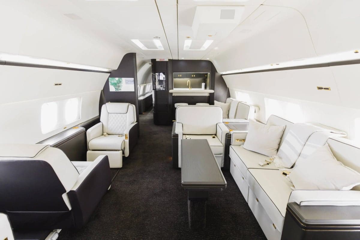 Interior view of the aircraft with white leather seating, a bar area, and a dark carpet.