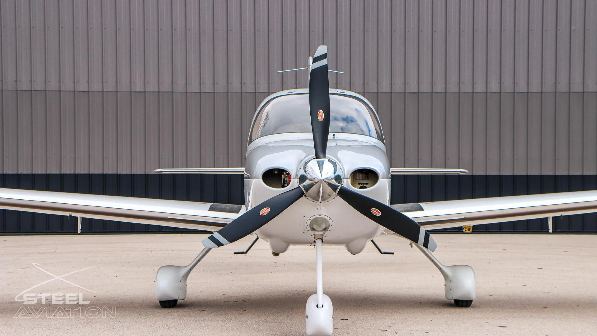 A close-up front view of the white and silver Cirrus SR22 aircraft, showing the propeller and nose.
