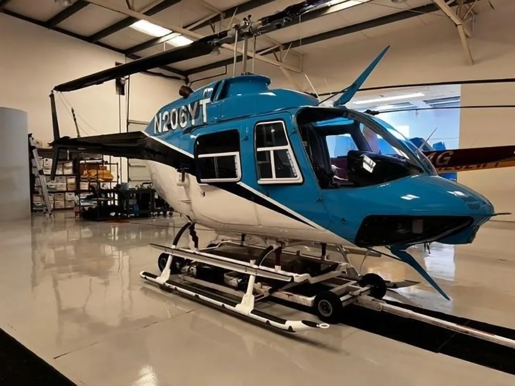 A blue and white Bell 206 helicopter, N206YT, on a dolly inside a hangar.