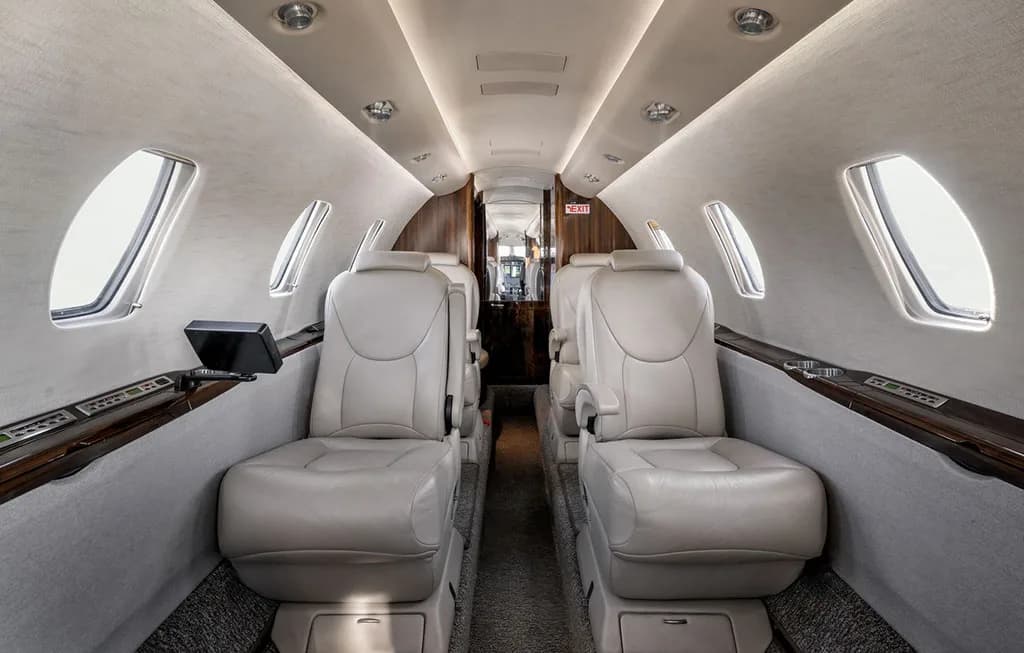 The luxurious cabin interior of the business jet features light-colored leather seats and a central aisle.
