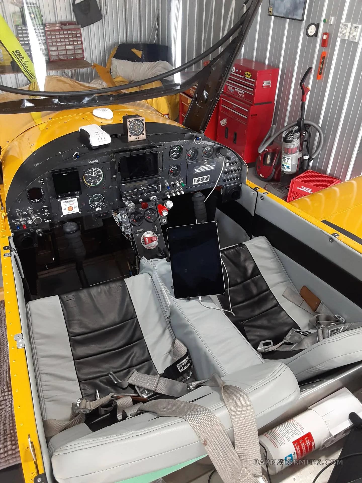 A yellow single-engine aircraft's cockpit and cabin interior with black and grey seats, an instrument panel, and an iPad mounted.