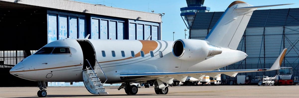 A white and gold Bombardier Challenger aircraft is parked on the tarmac with the entry stairs down.