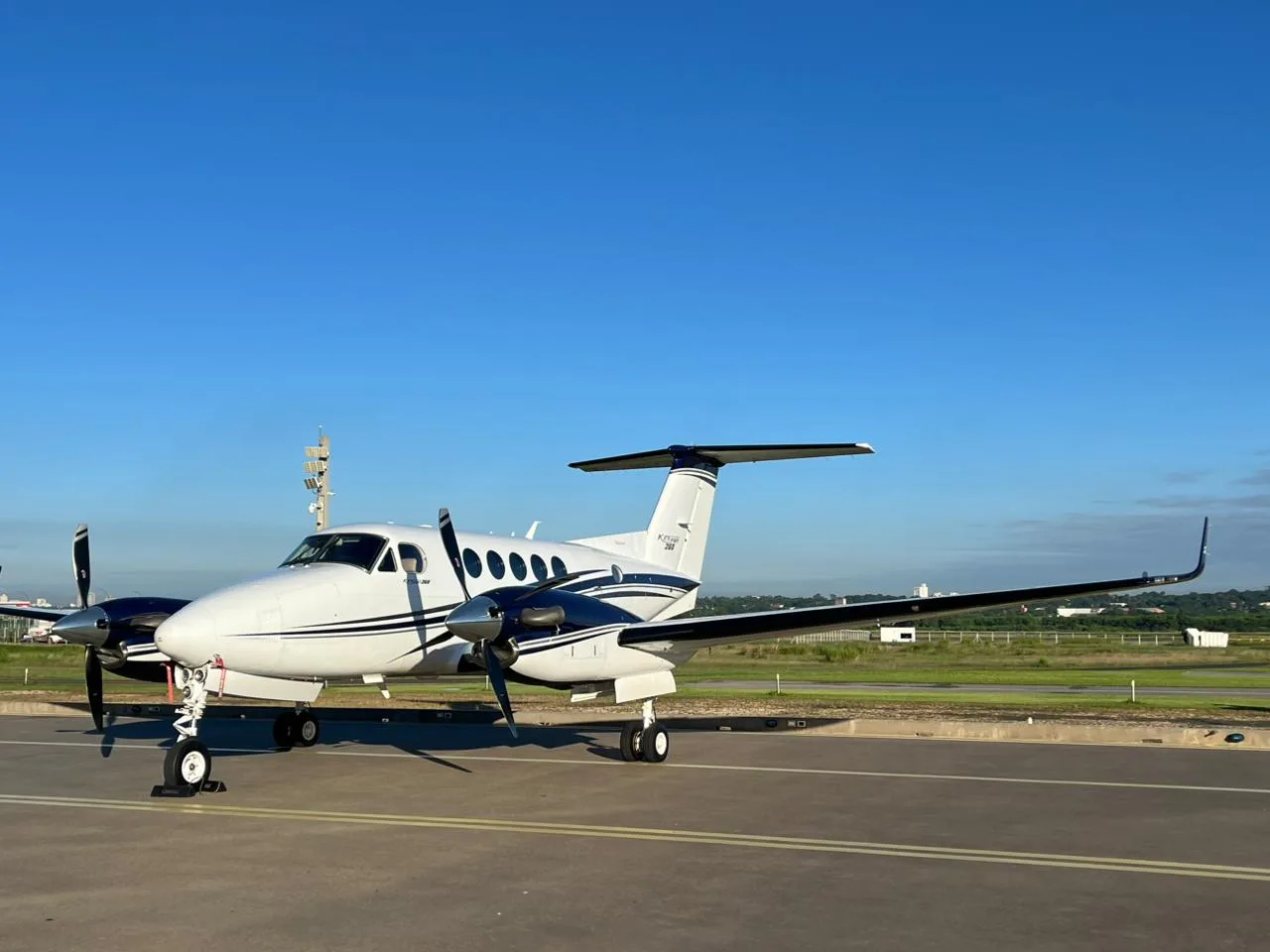 A white and dark blue twin-turboprop aircraft with propellers on an airport tarmac under a clear blue sky.