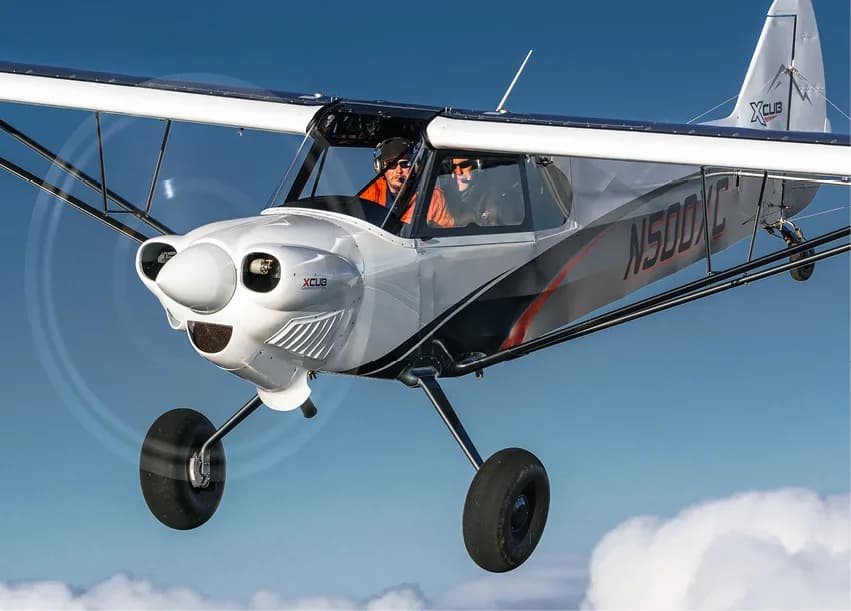 A silver and white XCub aircraft in flight.