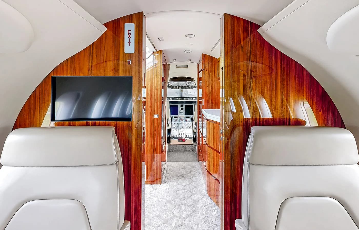 The private jet cabin interior features elegant wooden paneling, an 'EXIT' sign, and a view towards the cockpit.