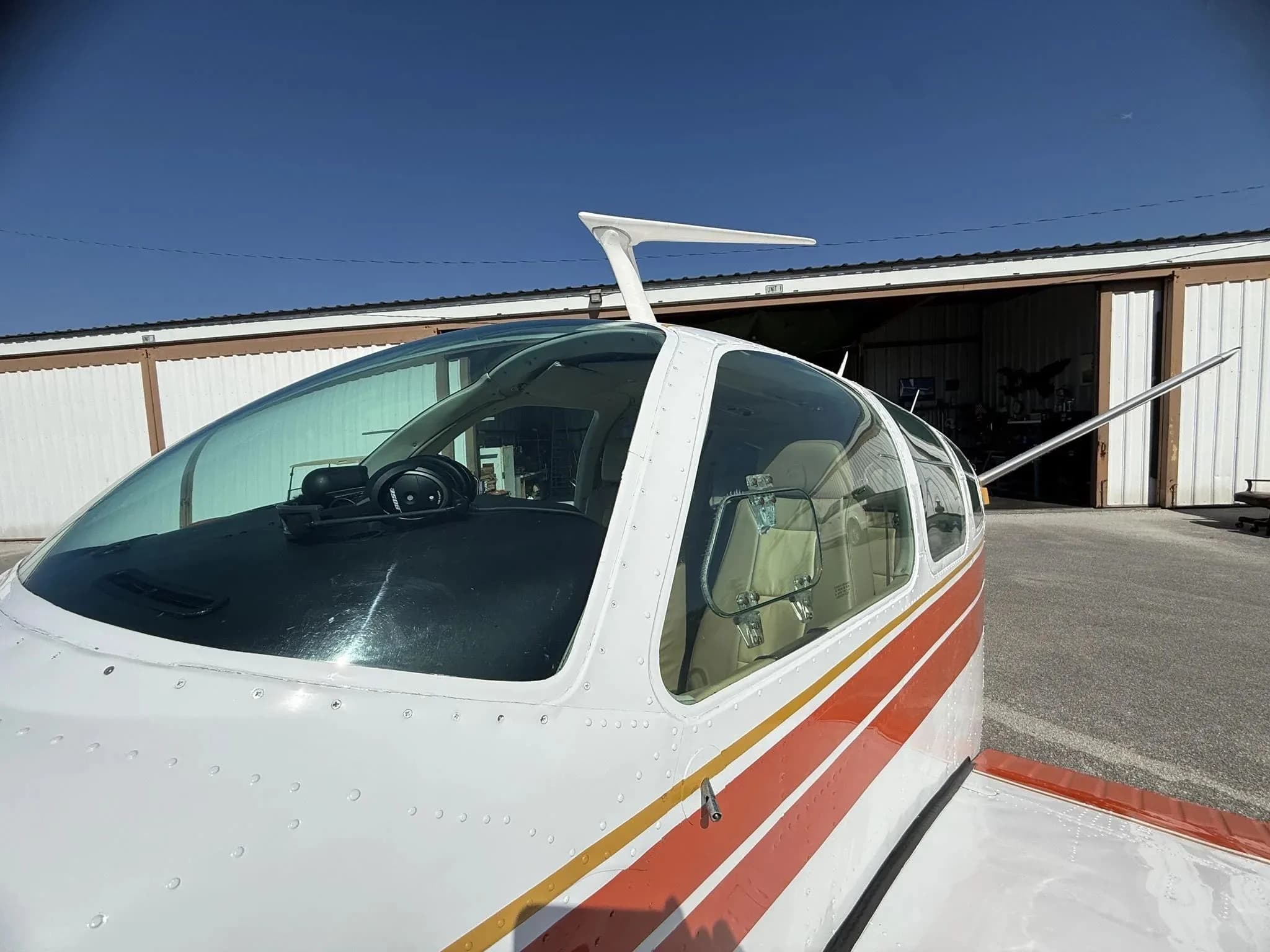 A close-up view of the clear canopy and front fuselage of a white and orange single-engine aircraft.